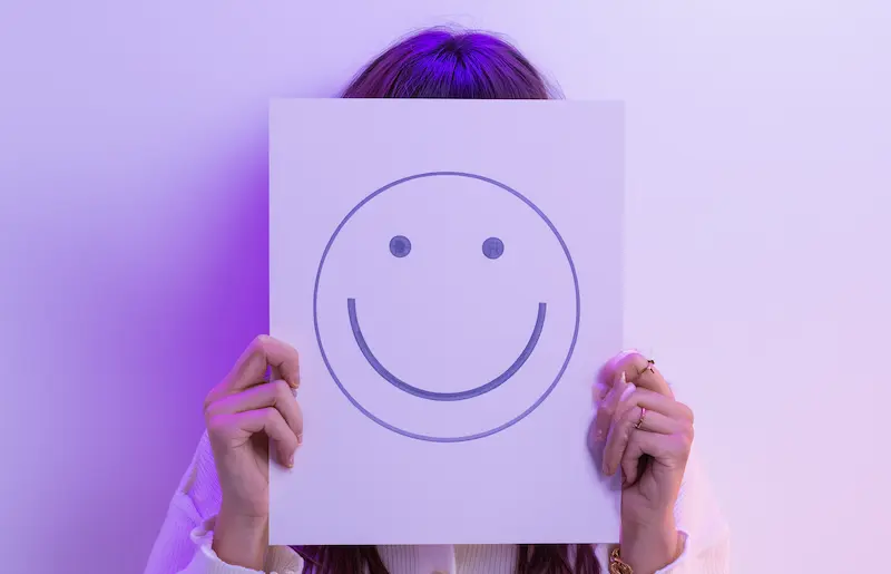 Persona sosteniendo un cartel con una carita feliz para representar confianza y felicidad. Diseño de sonrisa en Natural Smile