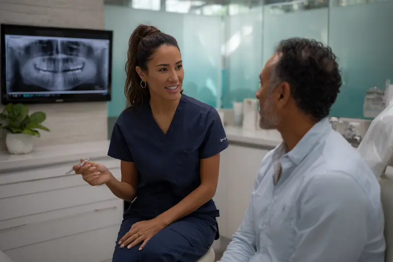 Odontóloga muestra una radiografía dental en pantalla a un paciente con dolor de muela para explicarle el diagnóstico antes de una endodoncia